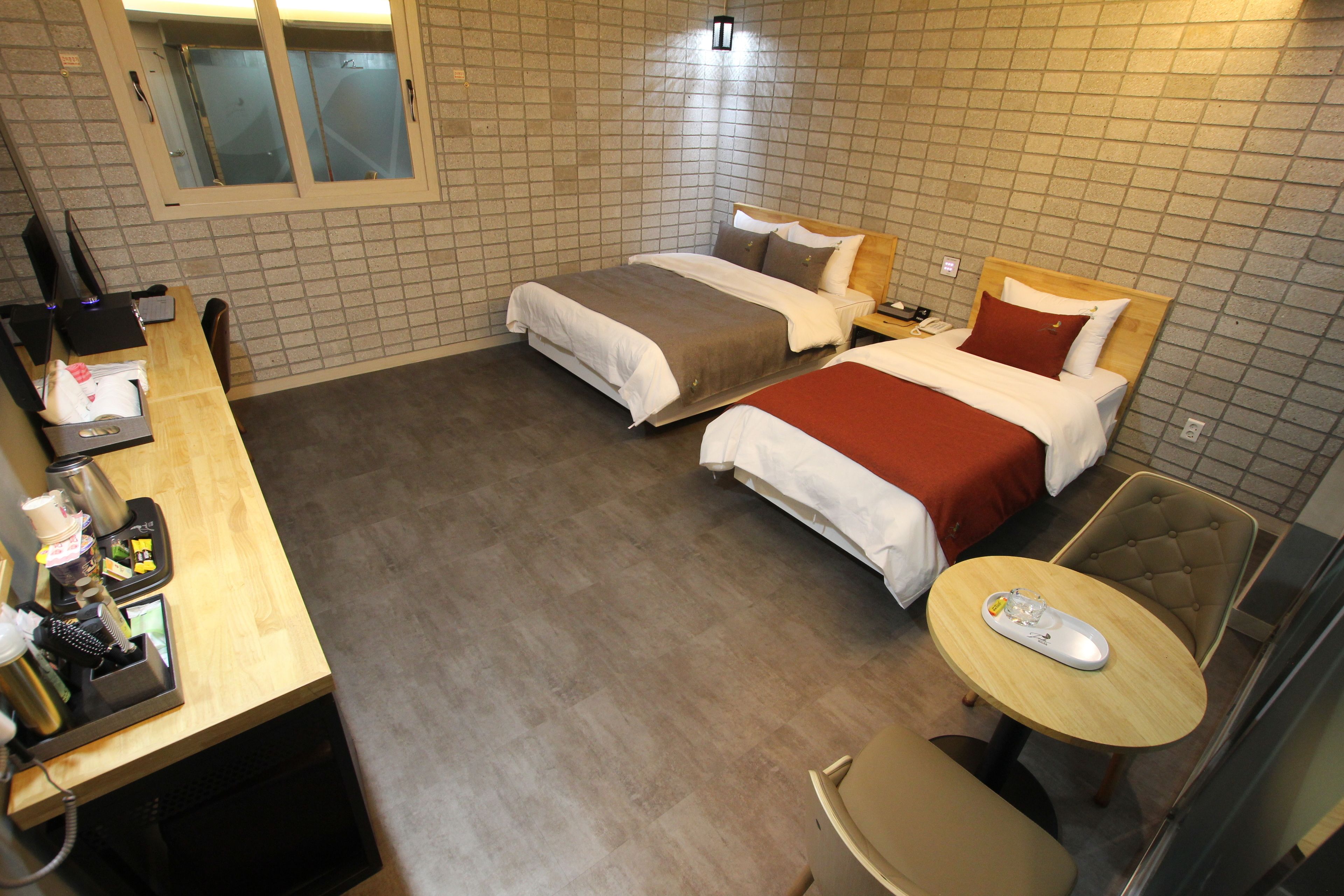 A hotel room with two beds, a desk with a computer and phone, a small round table, and a chair.