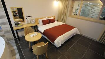 Ein Hotelzimmer mit einem Bett, einem Schreibtisch mit Telefon und Lampe, einem Sessel, einem kleinen Tisch und einer Badewanne.
