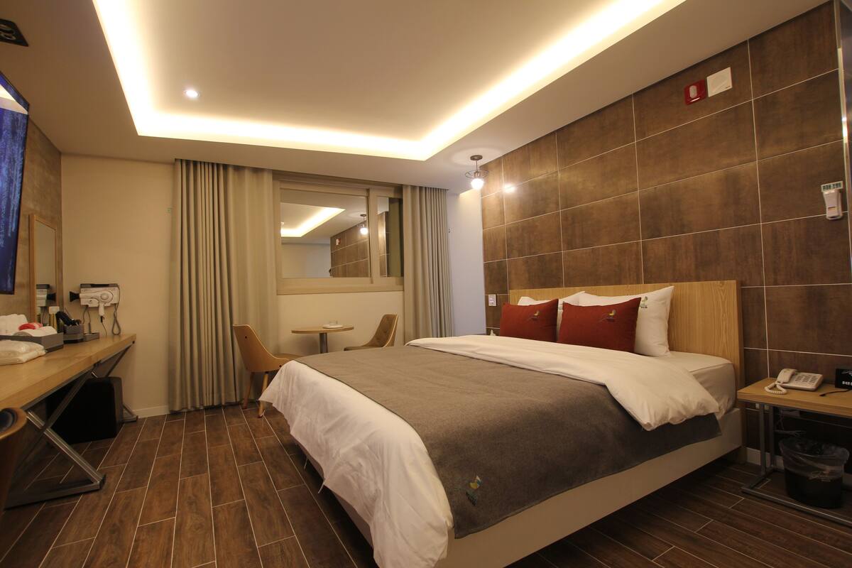 Habitación de hotel con una cama grande, un escritorio con teléfono, una silla, una mesita y un espejo.