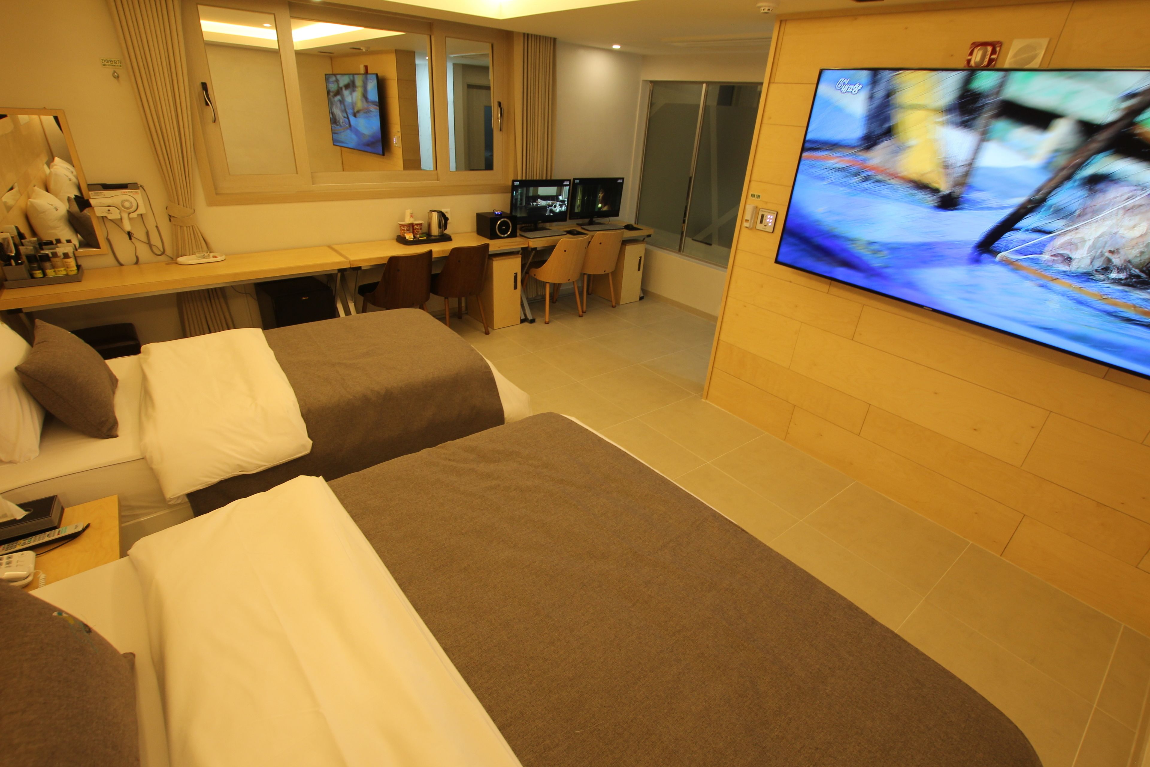 A hotel room with two beds, a desk with a computer, a TV, and a bathroom with a shower.