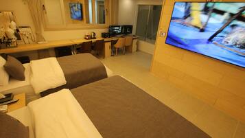 A hotel room with two beds, a desk with a computer, a TV, and a bathroom with a shower.