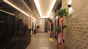A hotel lobby with a marble reception desk, potted plants, and a brick wall. - Jade Hotel Ulsan (Ulsan)