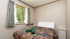 Een hotelkamer met een groot bed, een raam met gordijnen, een nachtkastje en een klein kastje.
