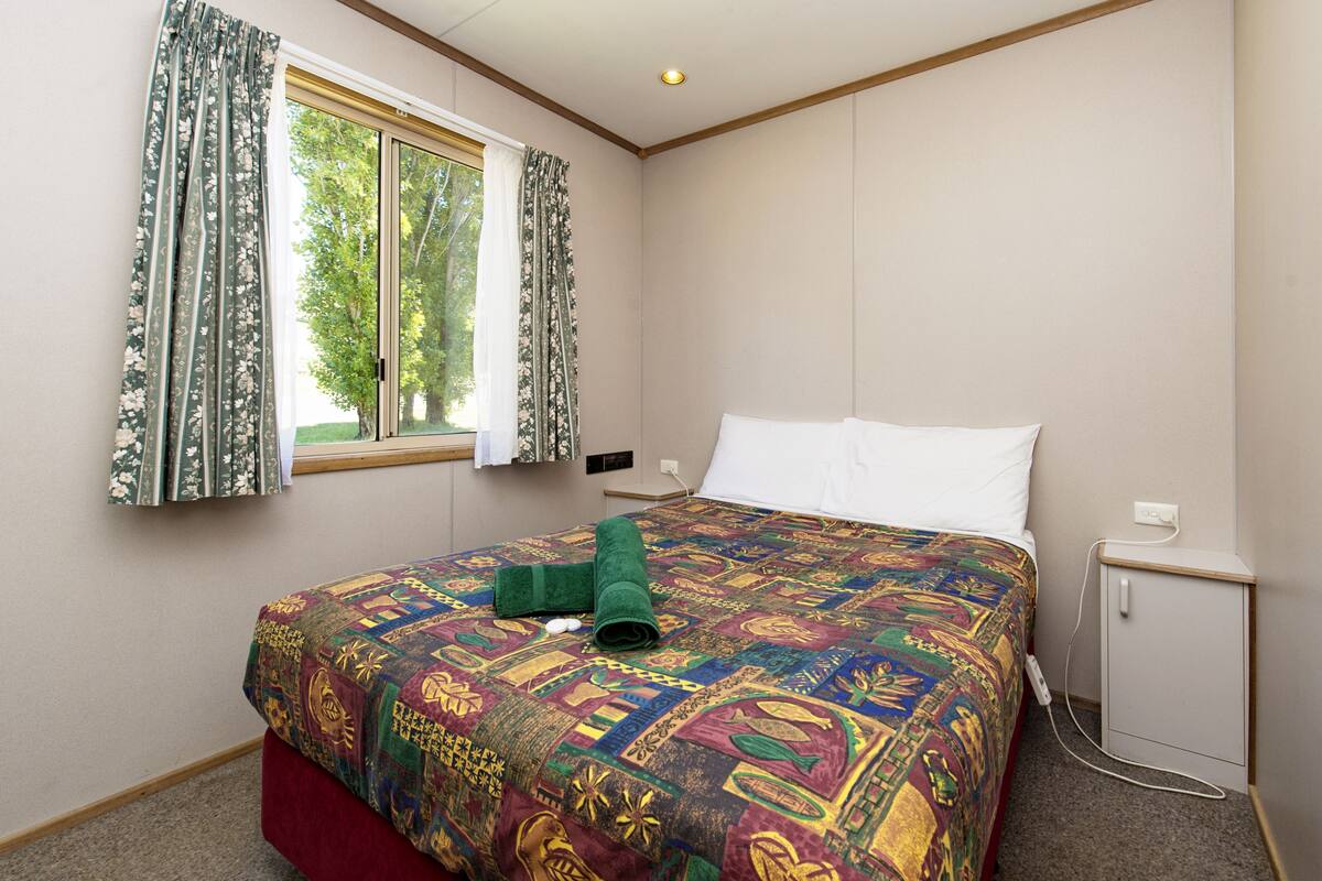 Ein Hotelzimmer mit einem großen Bett, einem Fenster mit Vorhängen, einem Nachttisch und einem kleinen Schrank.