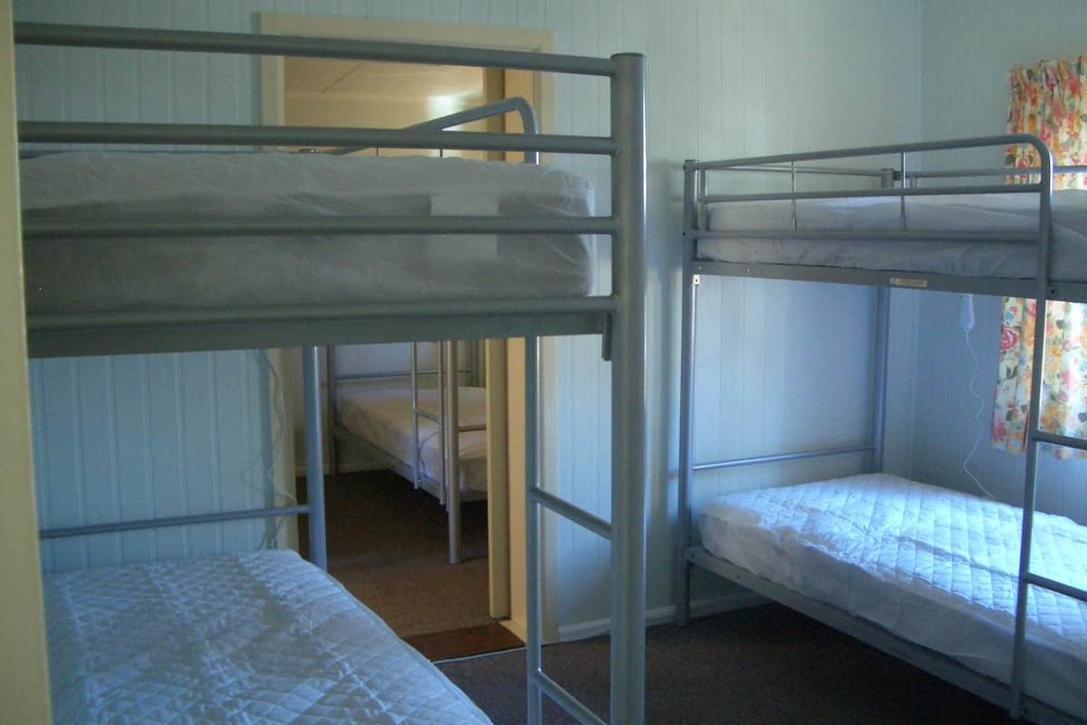 Ein Zimmer mit zwei Etagenbetten, einer Tür, die in ein weiteres Zimmer führt, und einem Fenster mit blumigen Vorhängen.
