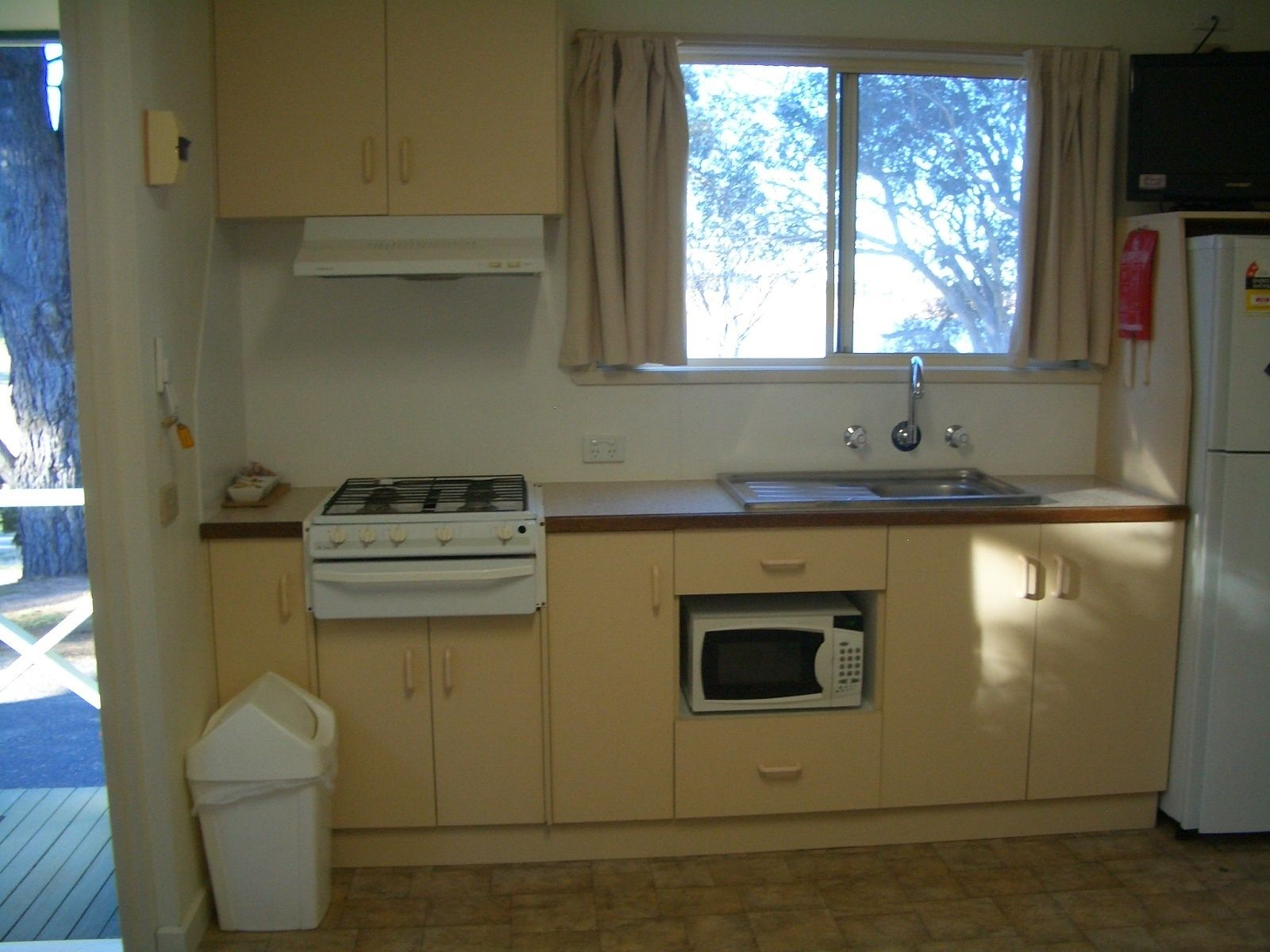 Una cocina compacta con estufa a gas, microondas, pileta y refrigerador.