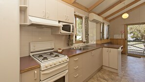 Een kleine keuken met een gasfornuis, magnetron en witte kastjes.