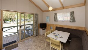 Een kamer met een houten plafond, een televisie op een kast, een tafel met stoelen en een bank.