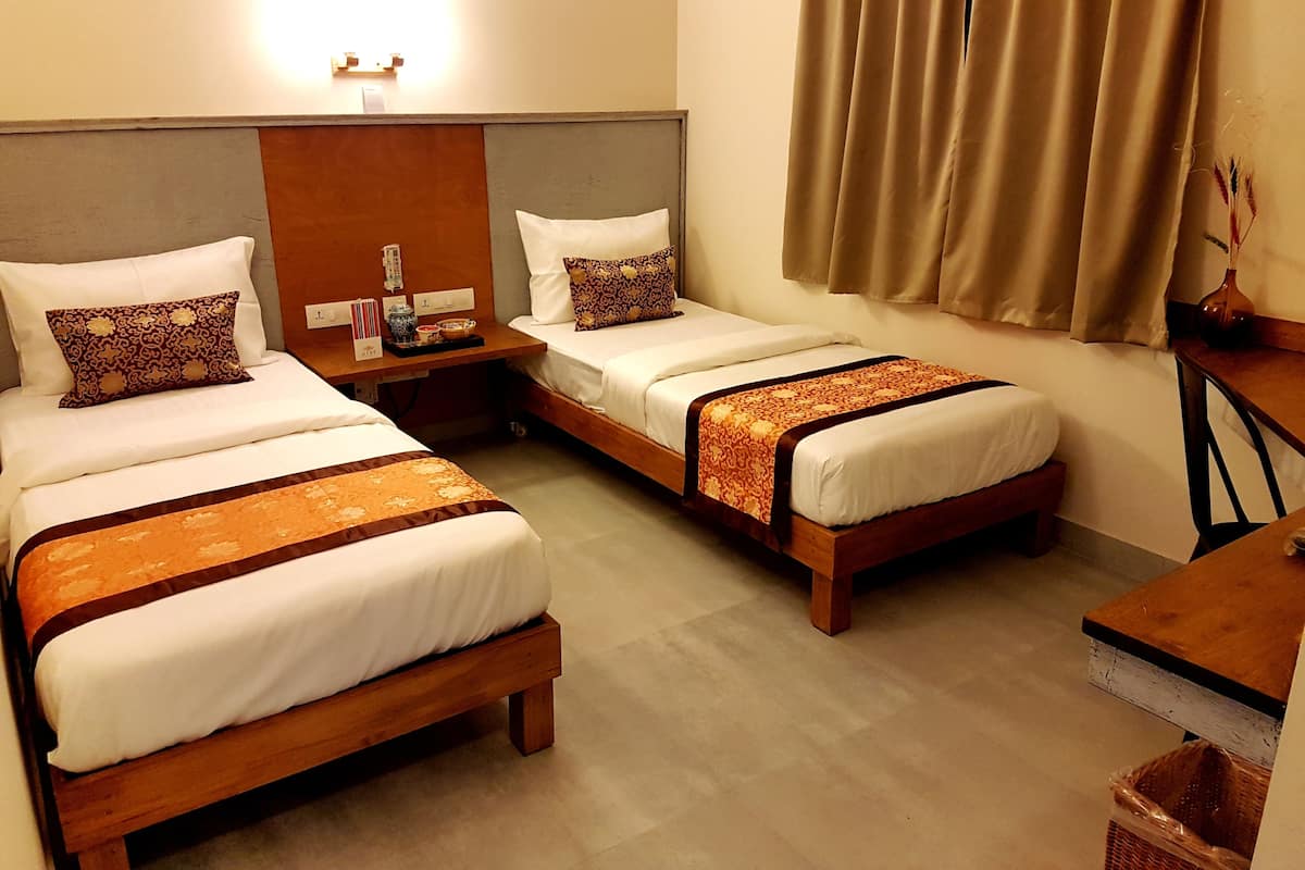 A hotel room with two single beds, a wooden nightstand, a small table, and a window with curtains.