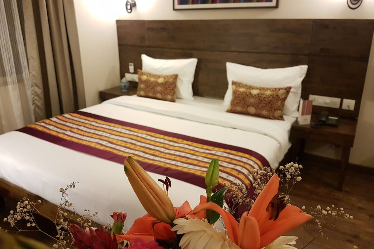 A hotel room with a large bed, a wooden headboard, two bedside tables, and a nightstand with a lamp.