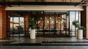 A hotel entrance with glass doors, potted plants, and a brick facade. - Rosa Malacca (Malacca City)