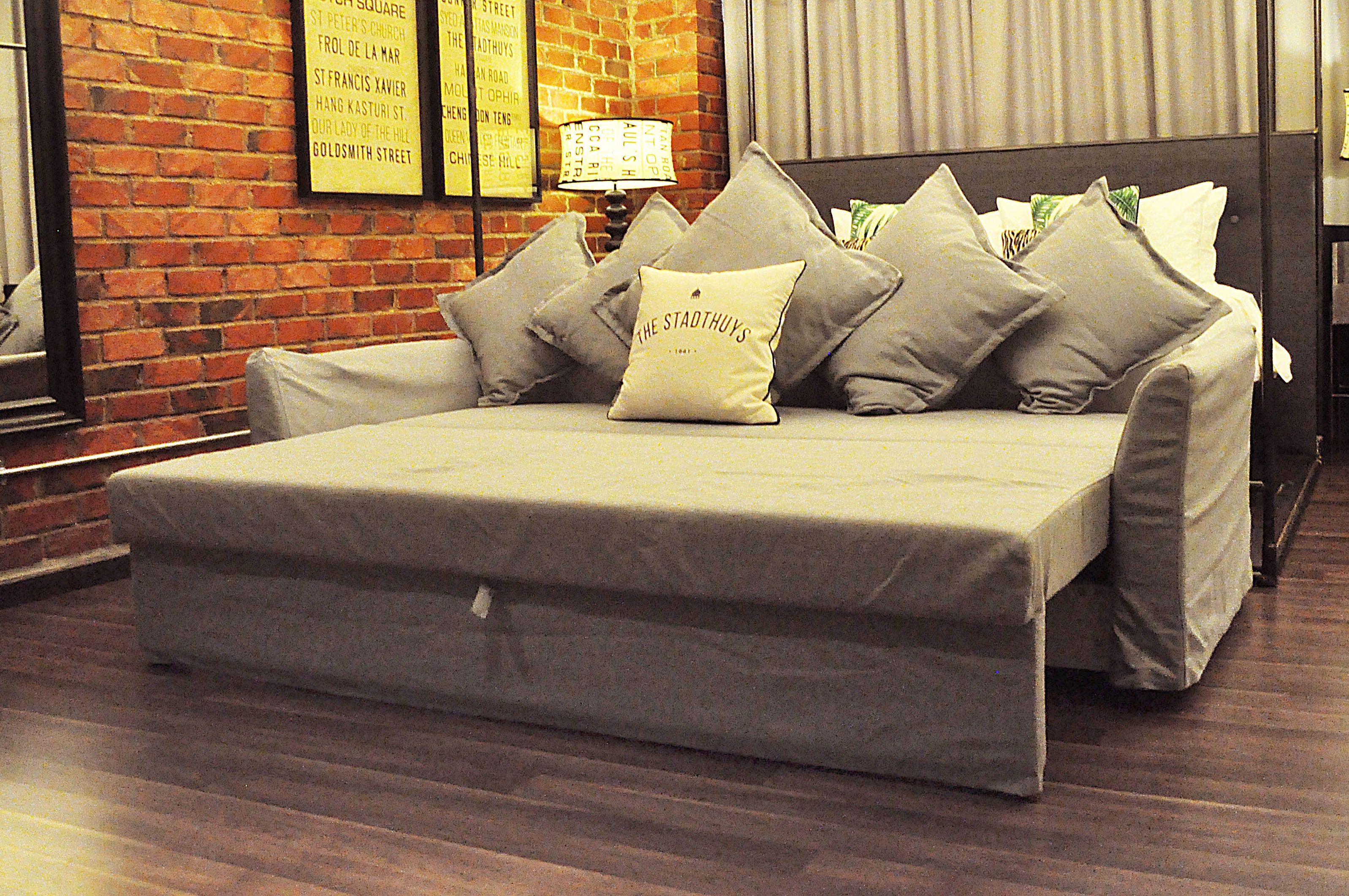 A neatly made bed with a grey mattress and multiple pillows, including one labeled "The Stadthuy's".