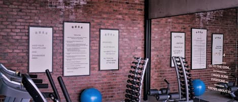 A gym with exercise equipment, a brick wall, and motivational posters.