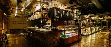 Una cafetería con mostrador, zona de estar y vitrina.
