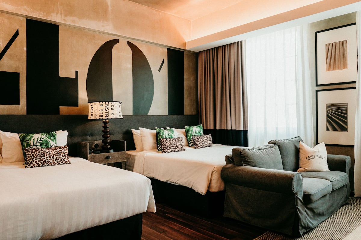 Ett hotellrum med två sängar, en soffa och ett stort, abstrakt konstverk på väggen.