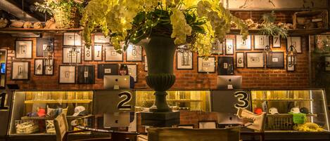 Een restaurantinterieur met een grote bloemenvaas, ingelijste foto's aan de muur en getabelde tafels.