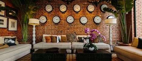Un salon chaleureux avec un mur en briques, plusieurs horloges, un canapé et une table basse.