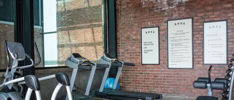 Une salle de sport équipée de tapis de course, d’un vélo d’appartement et d’appareils de musculation. Des affiches avec du texte sont accrochées aux murs.