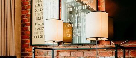 A room with a brick wall, a desk with two lamps, a chair, and a flat-screen TV mounted on the wall.