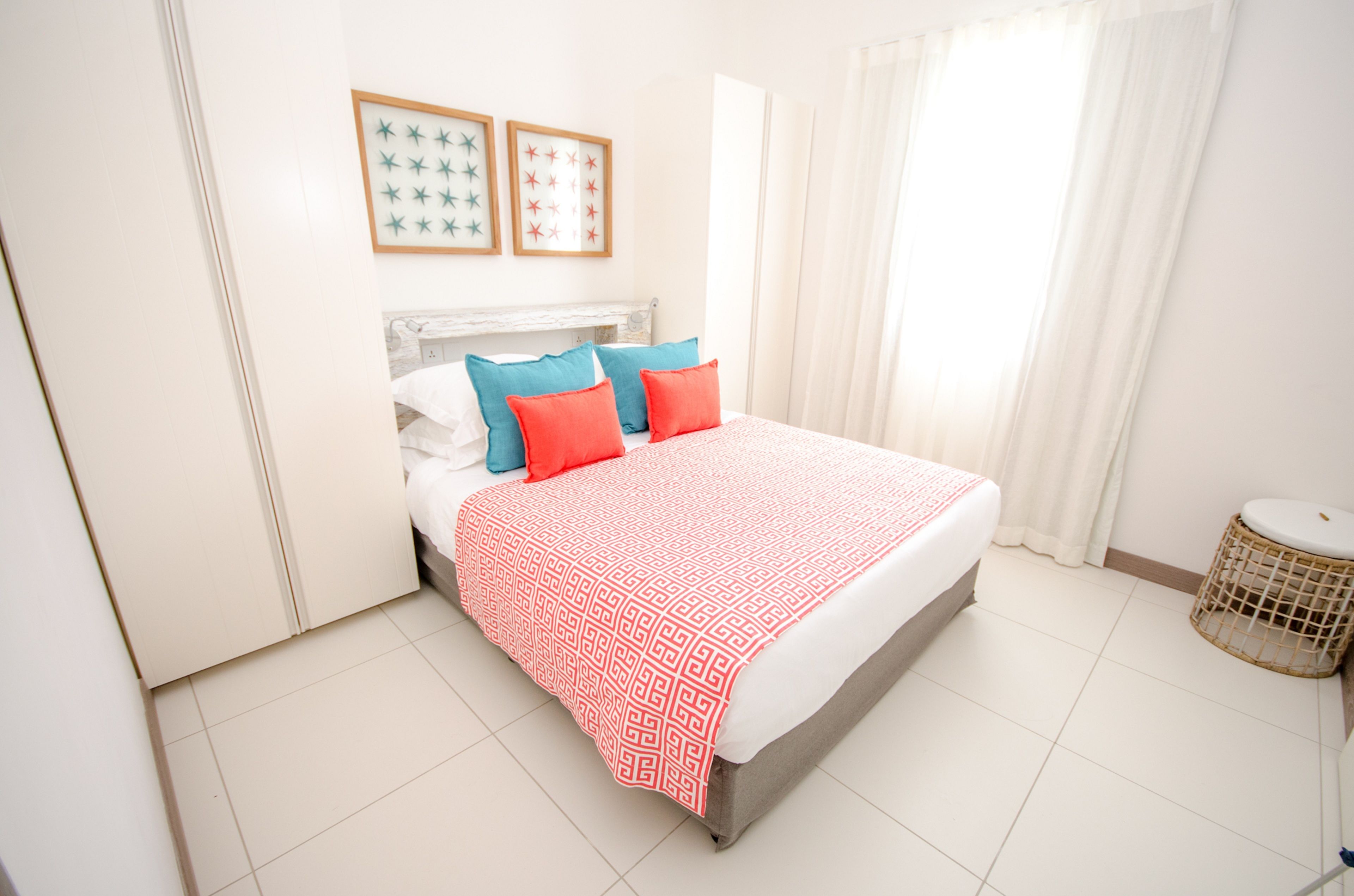 A neatly arranged bedroom with a bed, pillows, a bedside table, and a small round wicker stool.