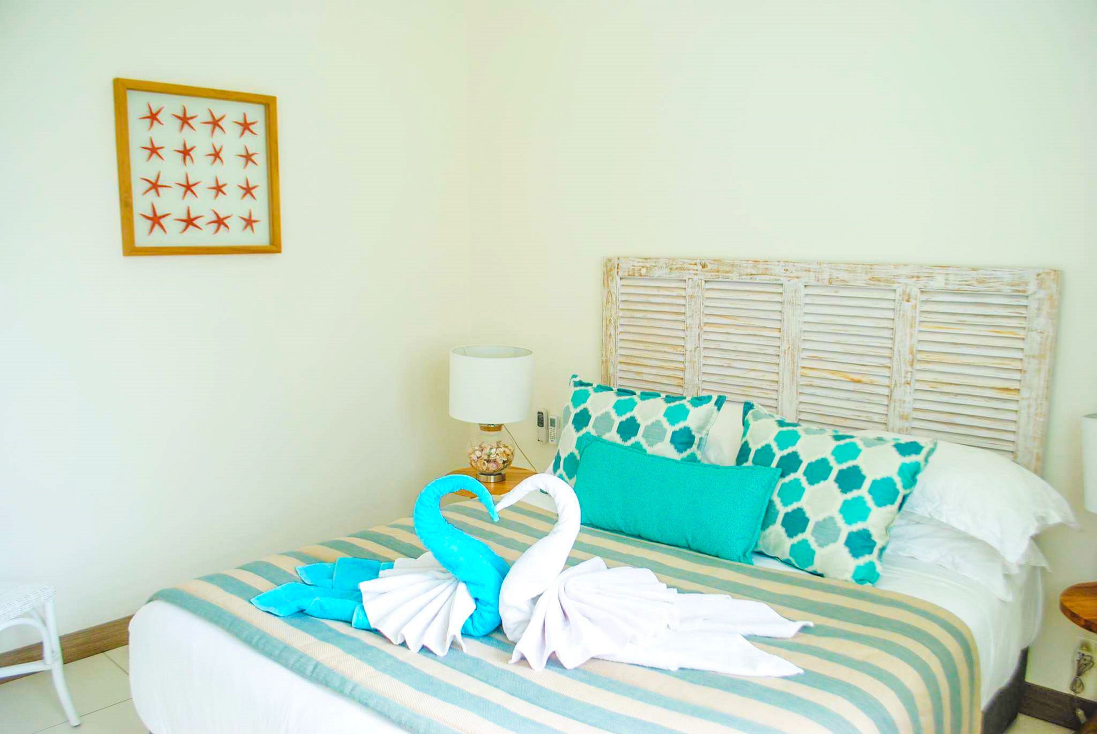 Una camera d'albergo con un letto, un quadro appeso al muro, una lampada e una finestra con persiane.
