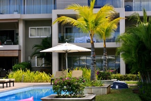 A pool area with lounge chairs, a palm tree, and a building with balconies.
