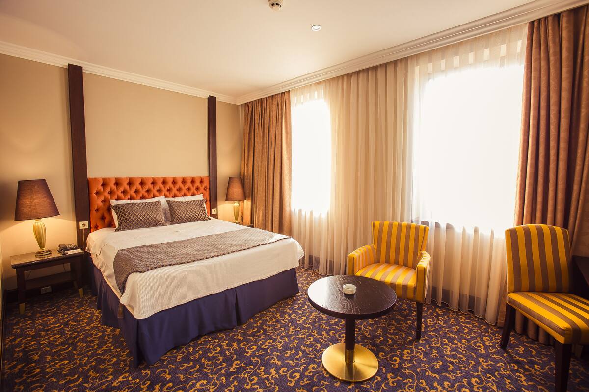 Ein Hotelzimmer mit einem großen Bett, zwei Sesseln, einem kleinen Tisch und einem Nachttisch mit Lampen.