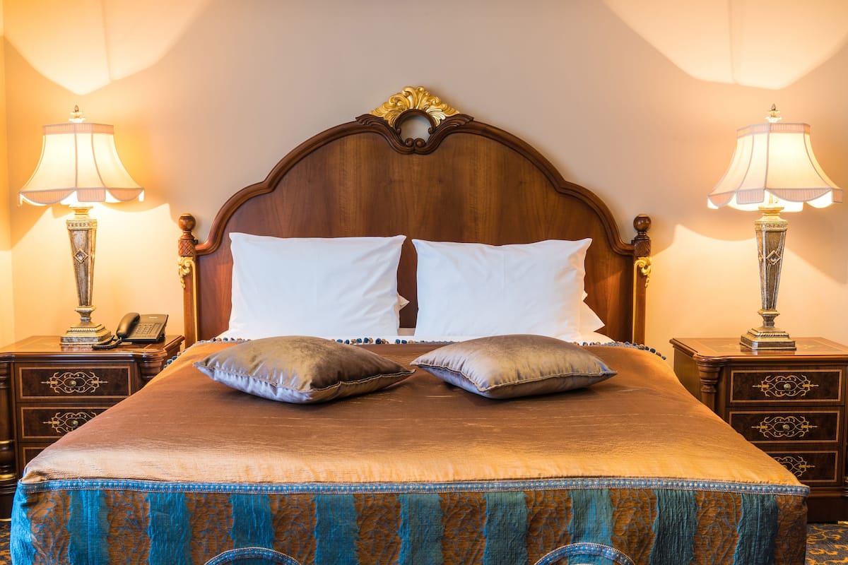 Ein großes Bett mit Holz-Kopfteil, zwei Nachttische mit Lampen und einer gemusterten Bettdecke.
