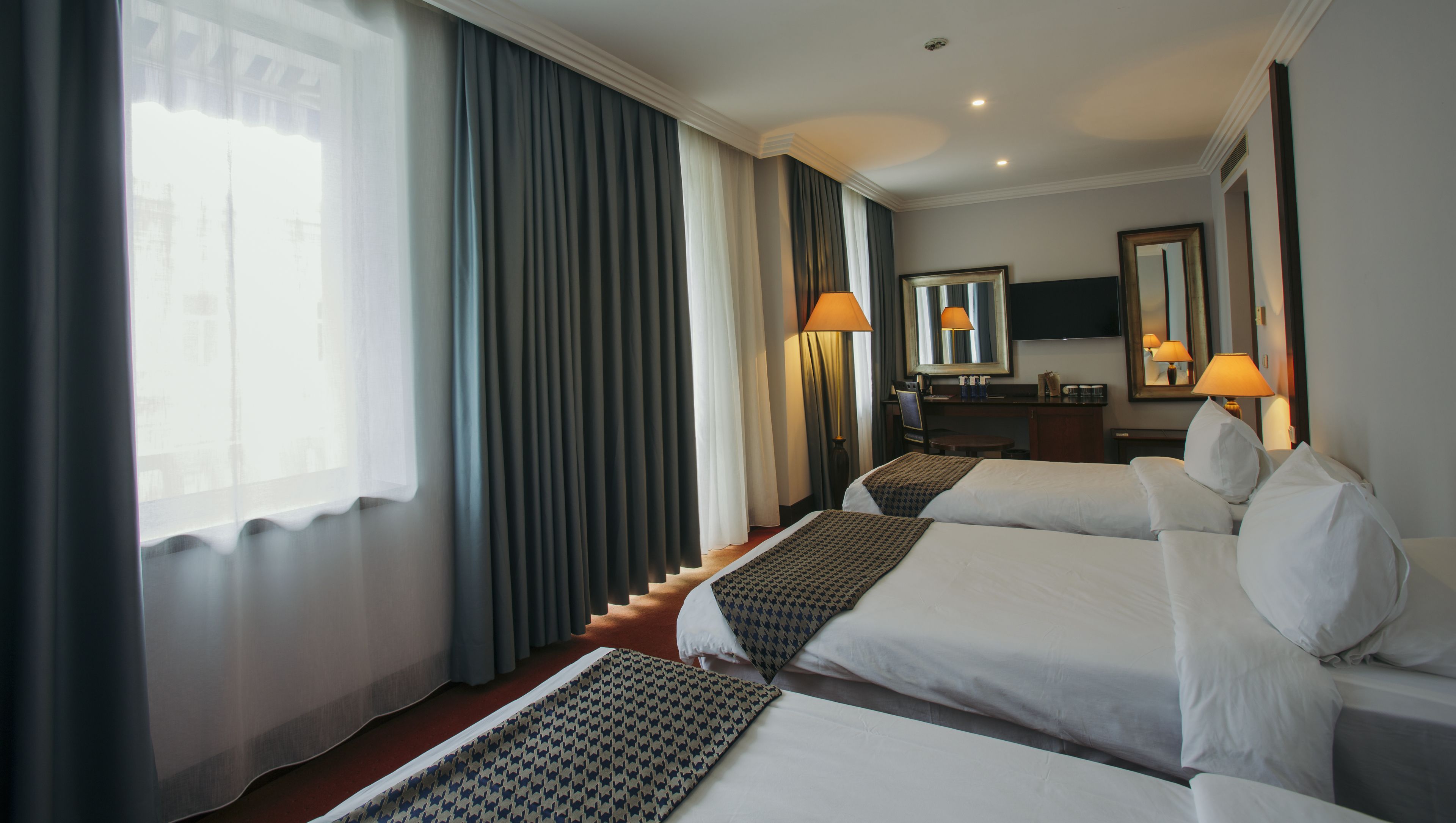 Habitación de hotel con dos camas, un escritorio, una silla, una lámpara y un espejo grande.