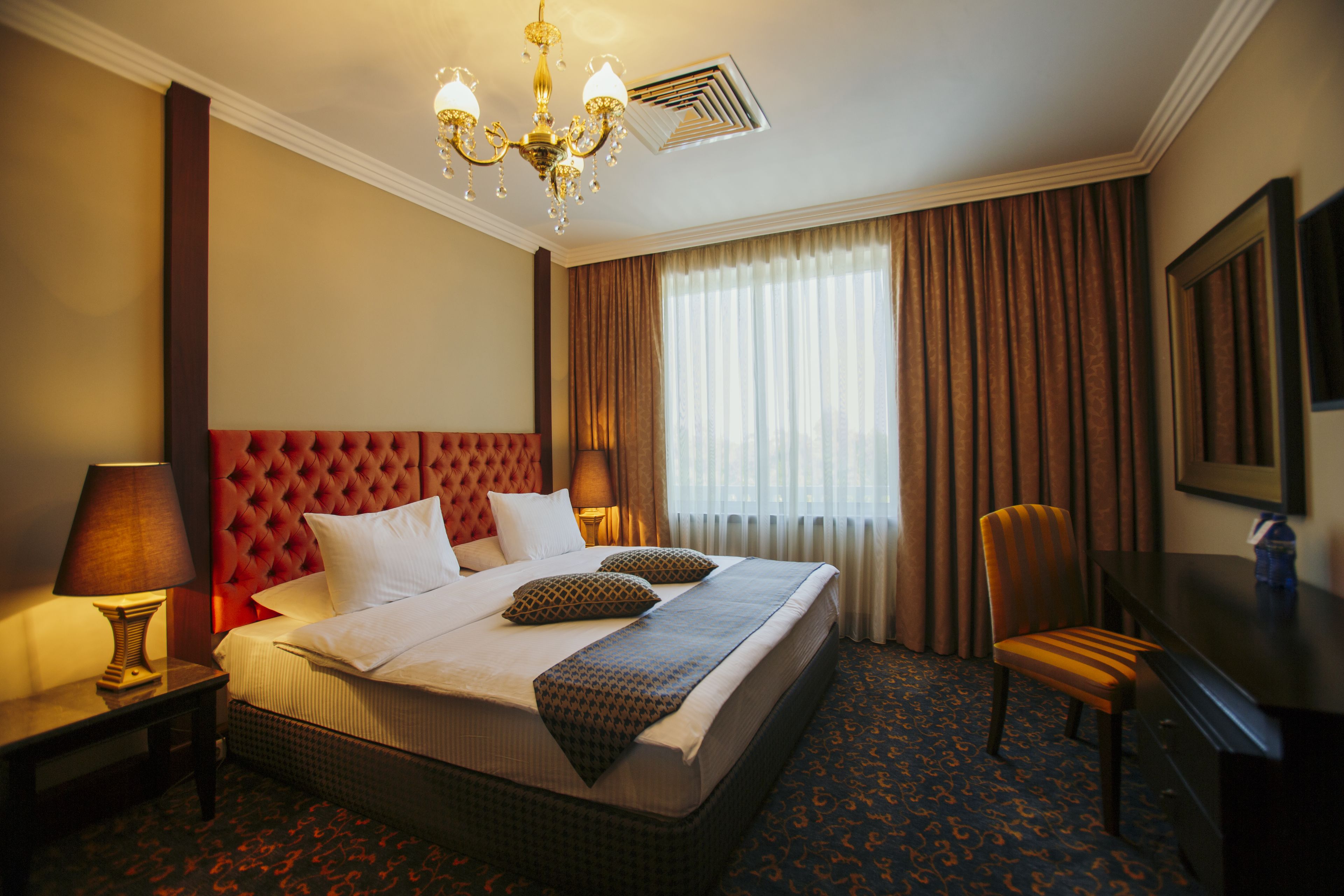A hotel room with a large bed, a desk, a chair, a TV, and a chandelier.