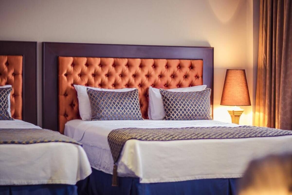 Ein Hotelzimmer mit zwei Betten, jeweils mit einem gepolsterten Kopfteil, weißer Bettwäsche und gemusterten Kissen.