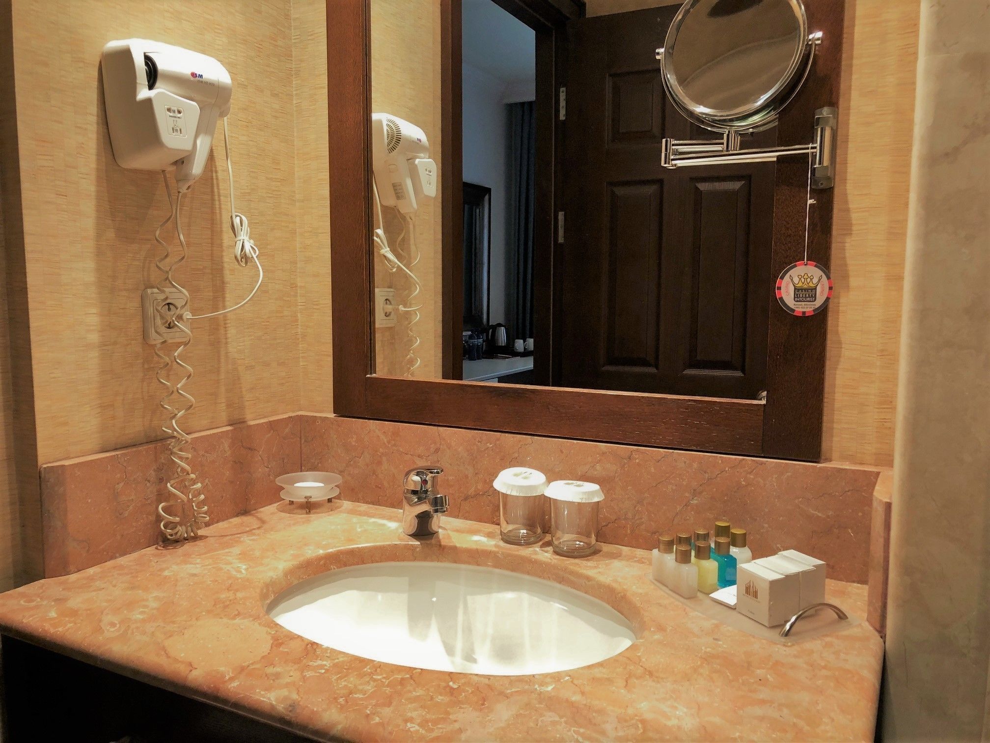 A bathroom with a marble sink, a hairdryer, a mirror, and toiletries on the counter.