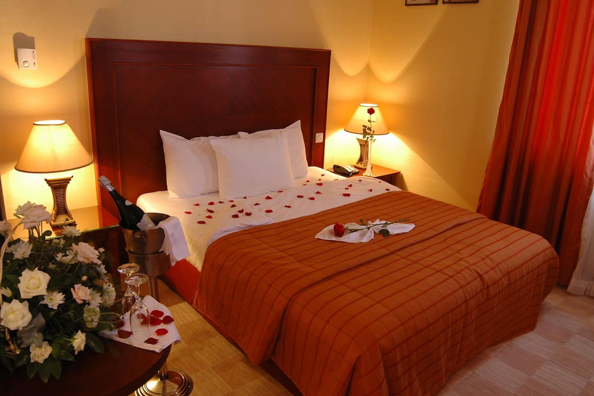 Ein Hotelzimmer mit einem großen Bett, zwei Nachttischlampen, einem Blumenstrauß und einer Champagnerflasche.
