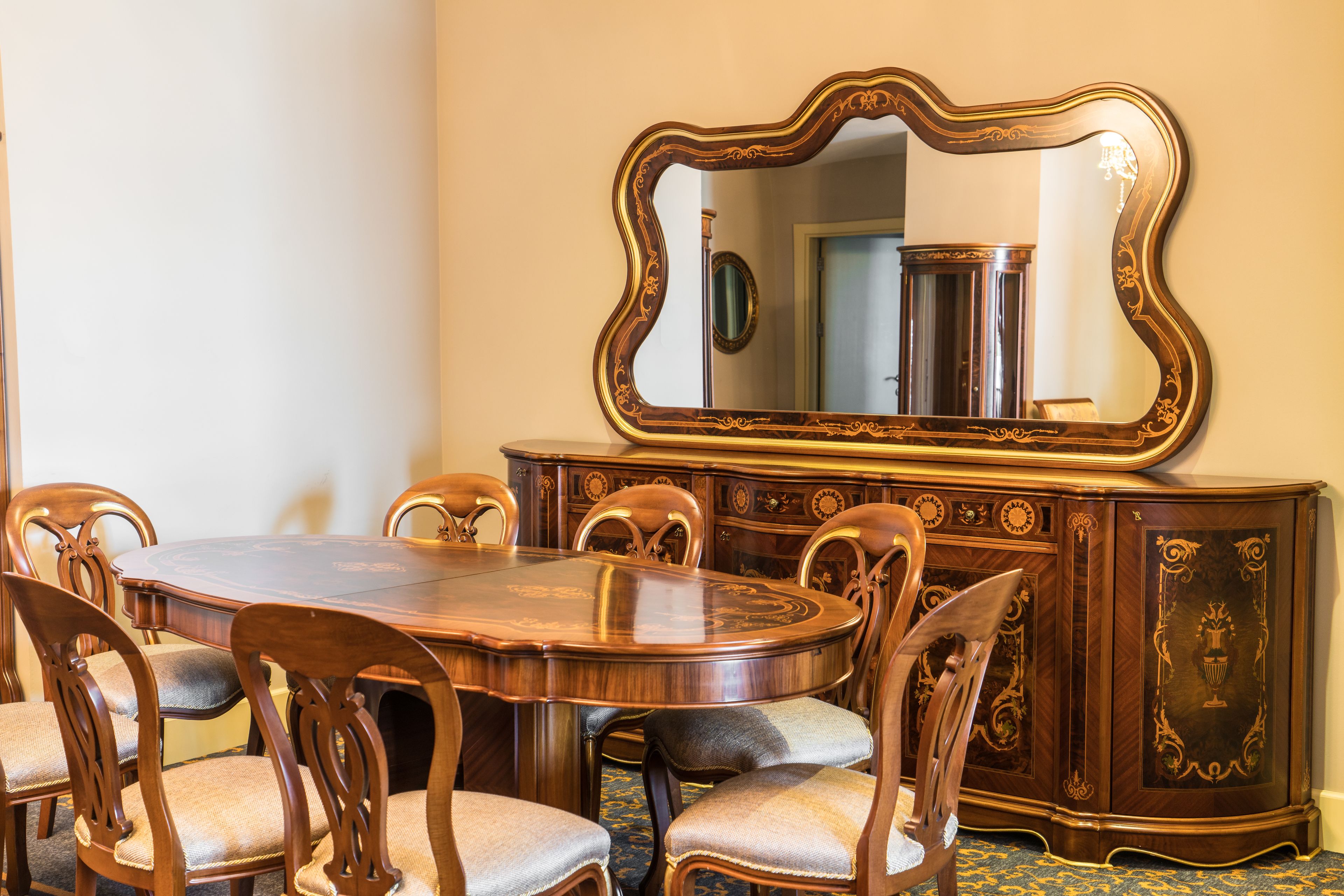 A dining room with a wooden table and chairs, a large ornate mirror, and a decorative wooden cabinet.