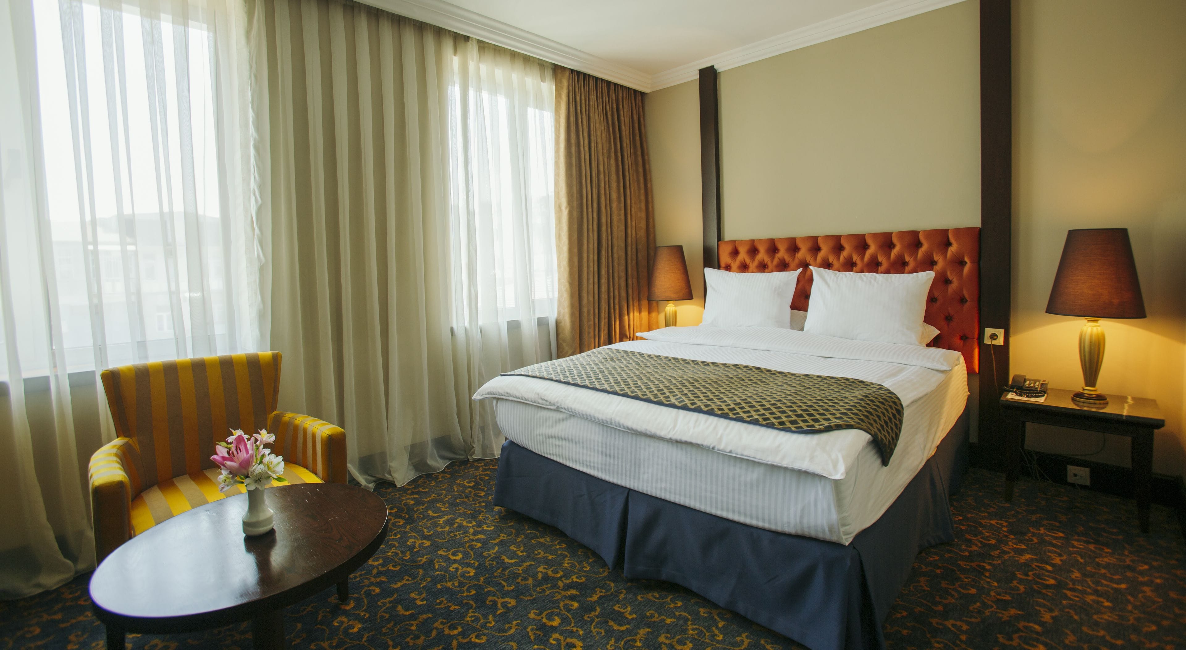 A hotel room with a large bed, a chair, a table, and a lamp.