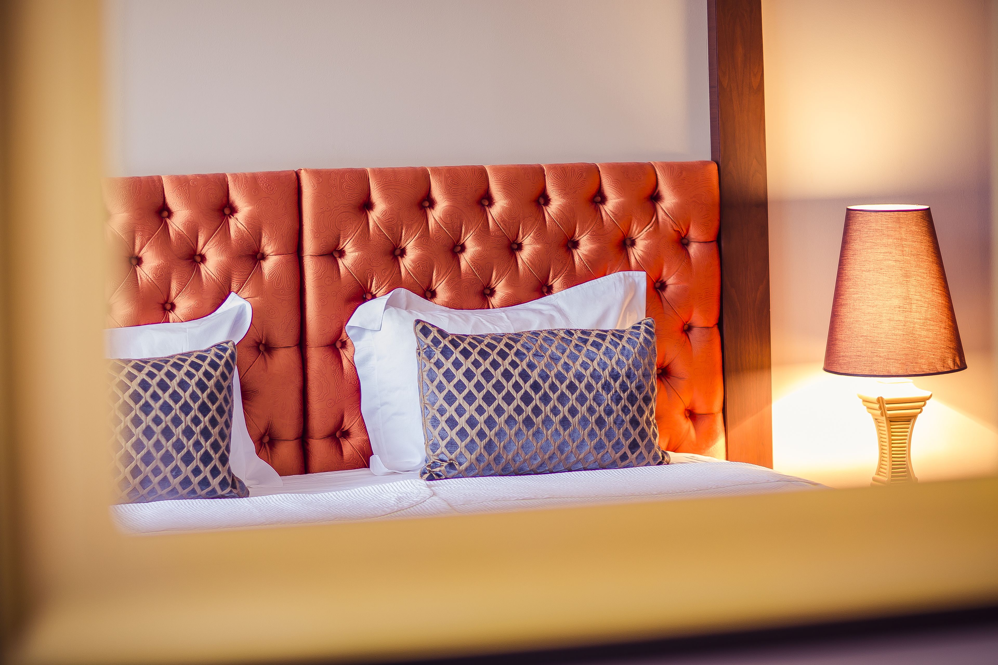 A bed with a tufted headboard, two patterned pillows, and a bedside lamp.