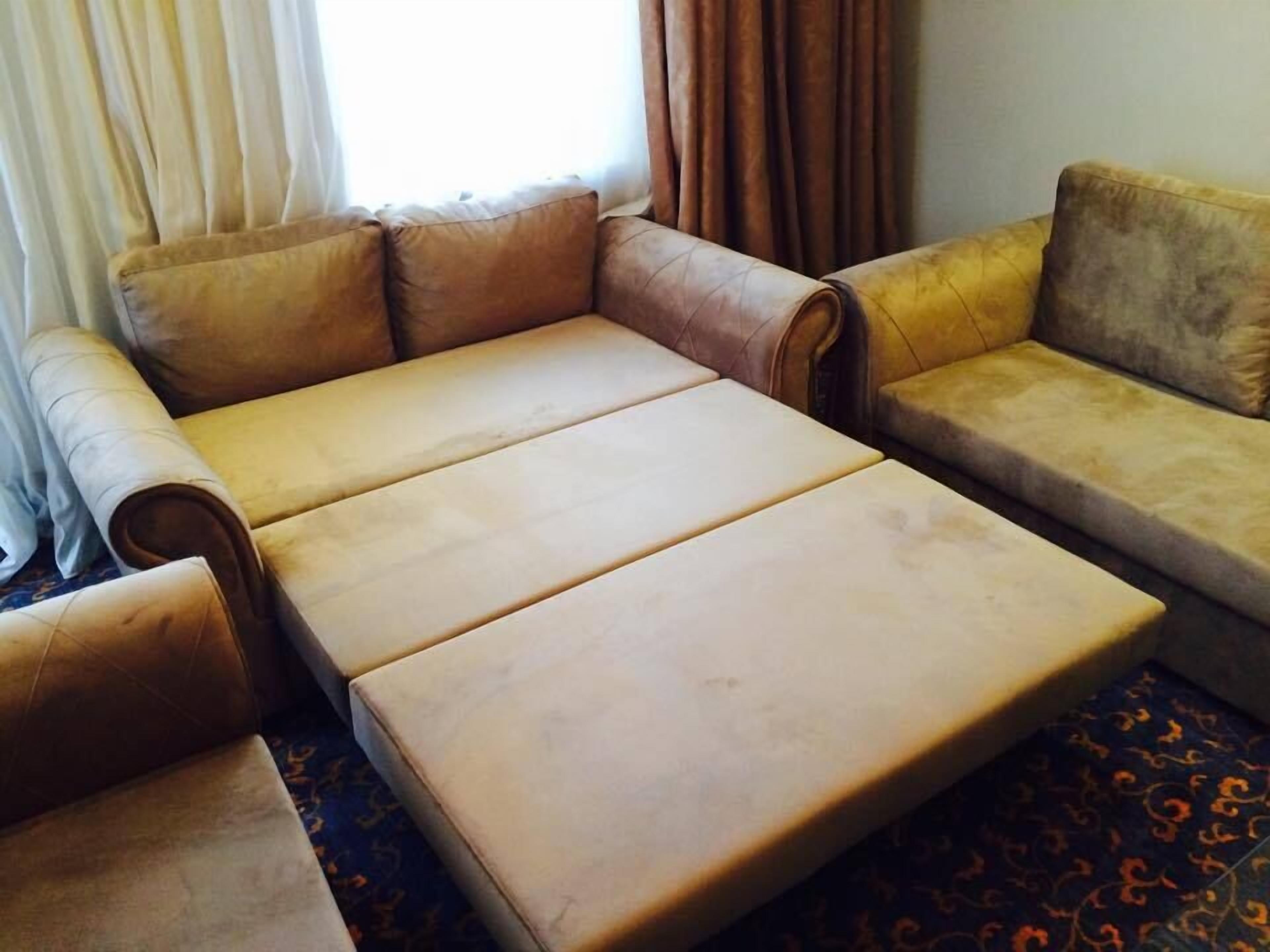 A sofa with a chaise lounge and a small table in a room with a patterned carpet.