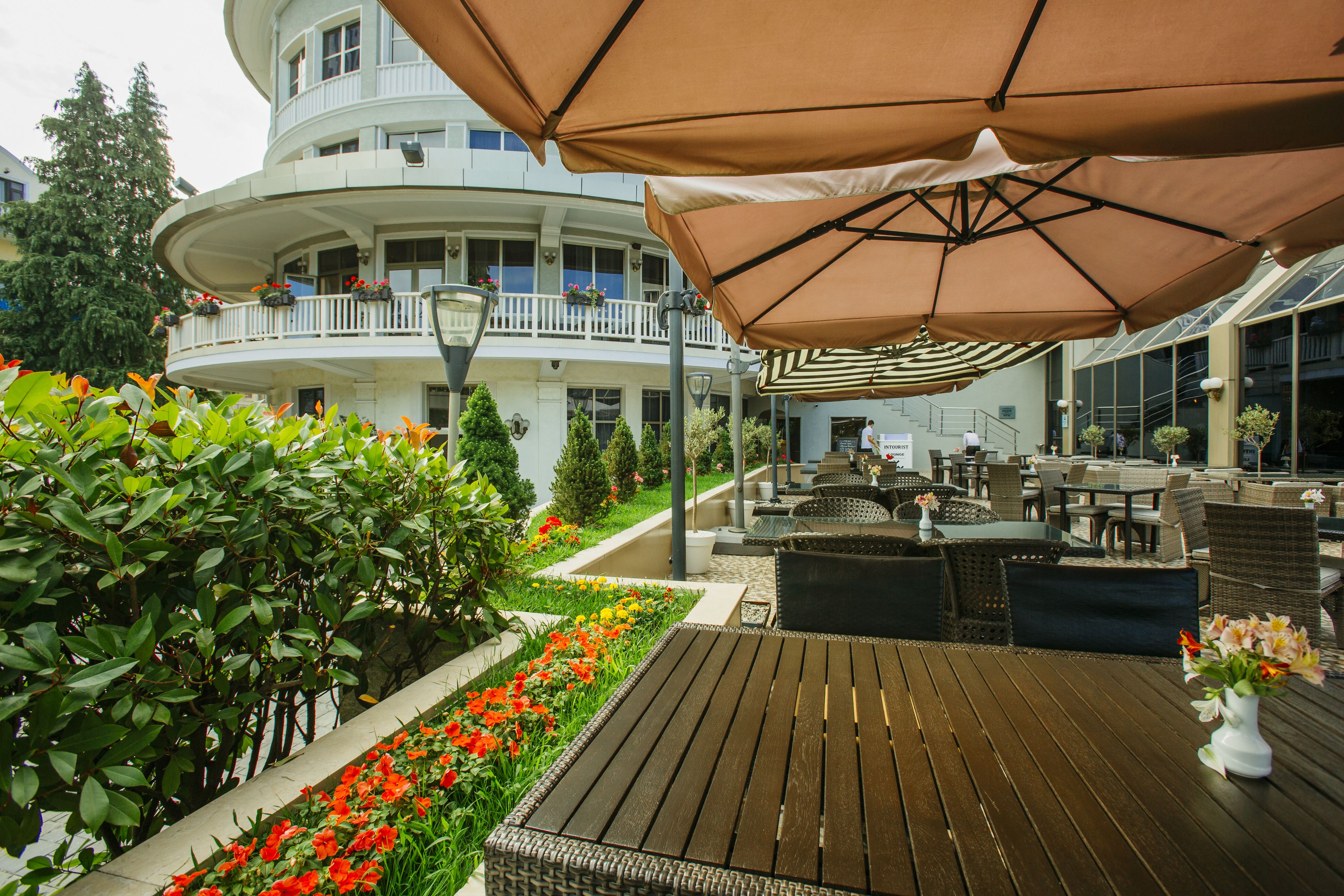 A wooden deck with outdoor seating, a white building with balconies, and a garden with red flowers.