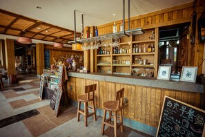 A bar area with wooden paneling, shelves with bottles and glasses, and two wooden stools. - Moonlit Sky Resort (Guilin)