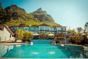 A hotel with a swimming pool, a mountain backdrop, and outdoor seating with umbrellas. - Moonlit Sky Resort (Guilin)