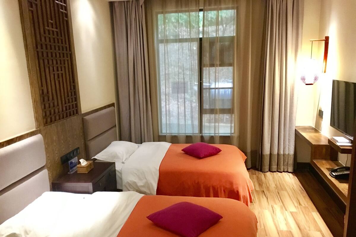 A hotel room with two beds, a TV, a desk, and a window with curtains.