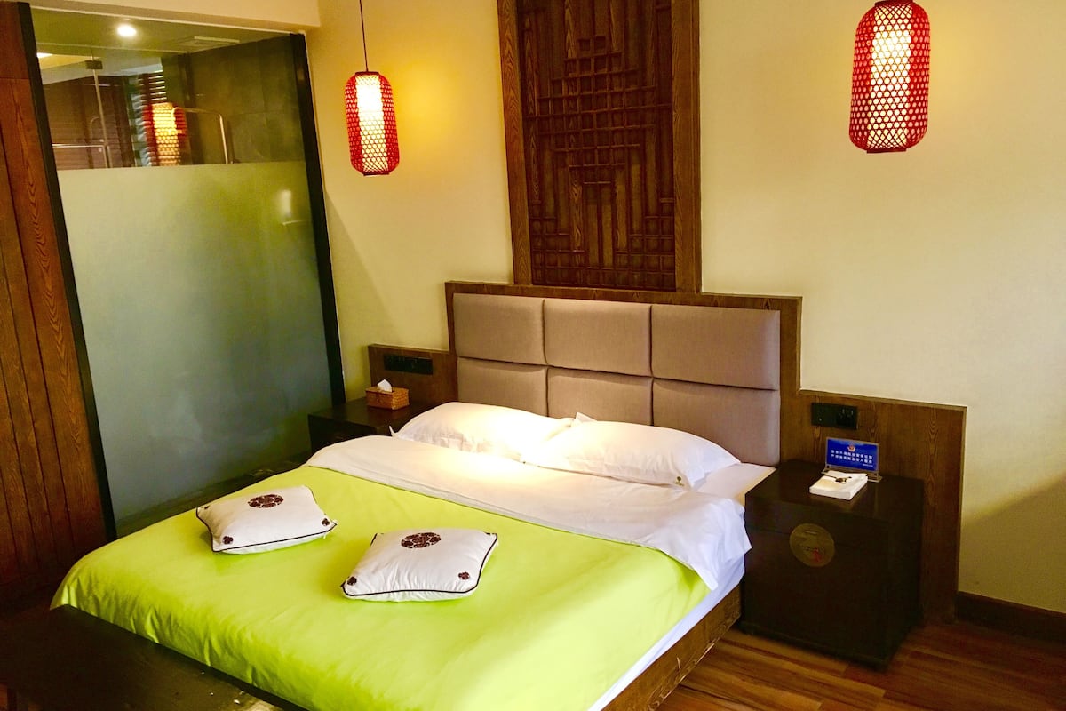 A hotel room with a bed, two nightstands, a wooden headboard, and two red wall lamps.