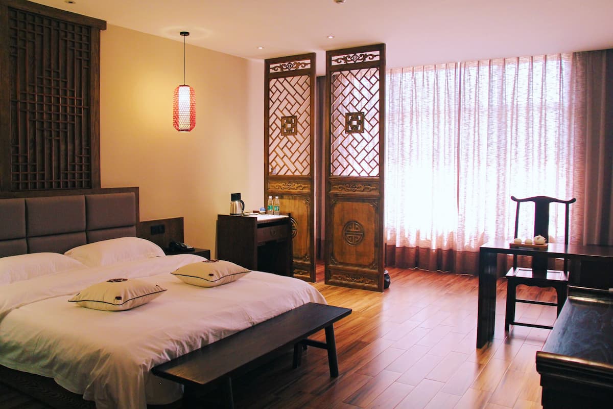 A hotel room with a large bed, a desk, a chair, and a piano.