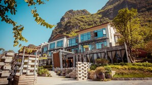 A modern building with large windows and a stone facade, surrounded by greenery and a mountainous backdrop. - Moonlit Sky Resort (Guilin)
