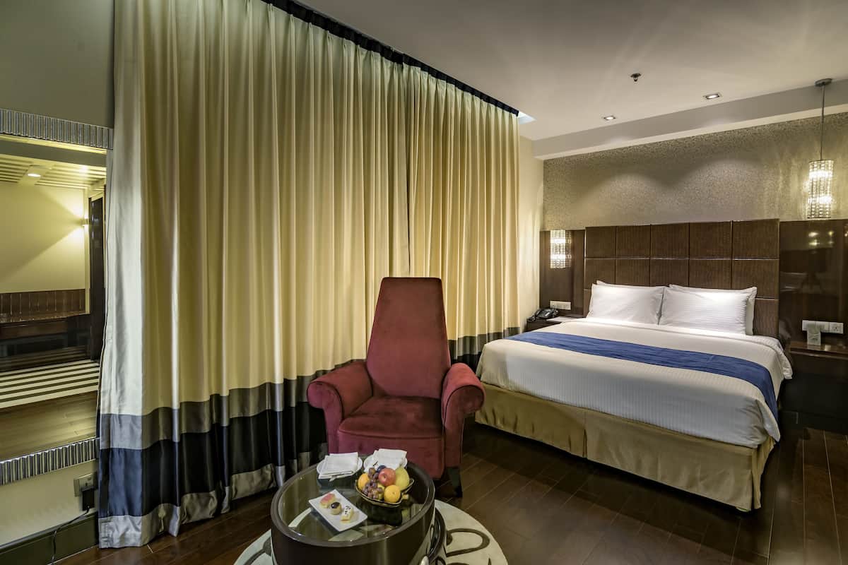 Ein Hotelzimmer mit einem Bett, einem roten Sessel, einem Glastisch mit Früchten und Vorhängen.