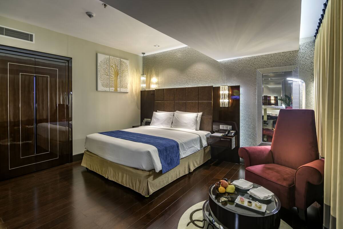 Ein Hotelzimmer mit einem Bett, einem Schreibtisch, einem Stuhl, einem runden Tisch mit Früchten und einer Ablagefläche sowie einem Kleiderschrank.