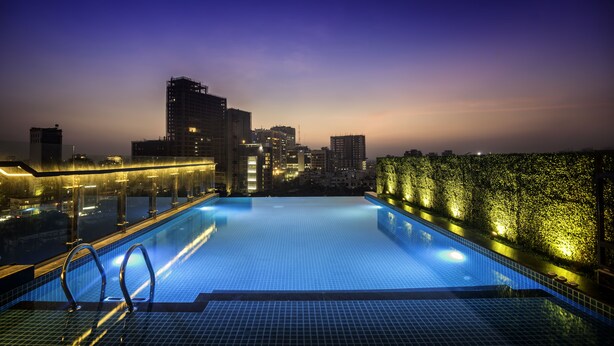 A rooftop infinity pool with city skyline views, illuminated poolside area, and a glass balustrade. - The Raintree Dhaka (Dhaka)