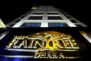 Un letrero de hotel con el nombre 'The Rainforest Dhaka' iluminado en dorado.