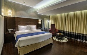 A hotel room with a large bed, a desk, a chair, and a small table with a fruit bowl. - The Raintree Dhaka (Dhaka)