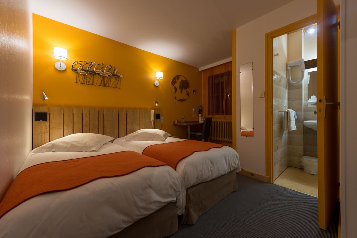 A hotel room with two beds, a wooden headboard, a globe decoration, and a bathroom visible through an open door.